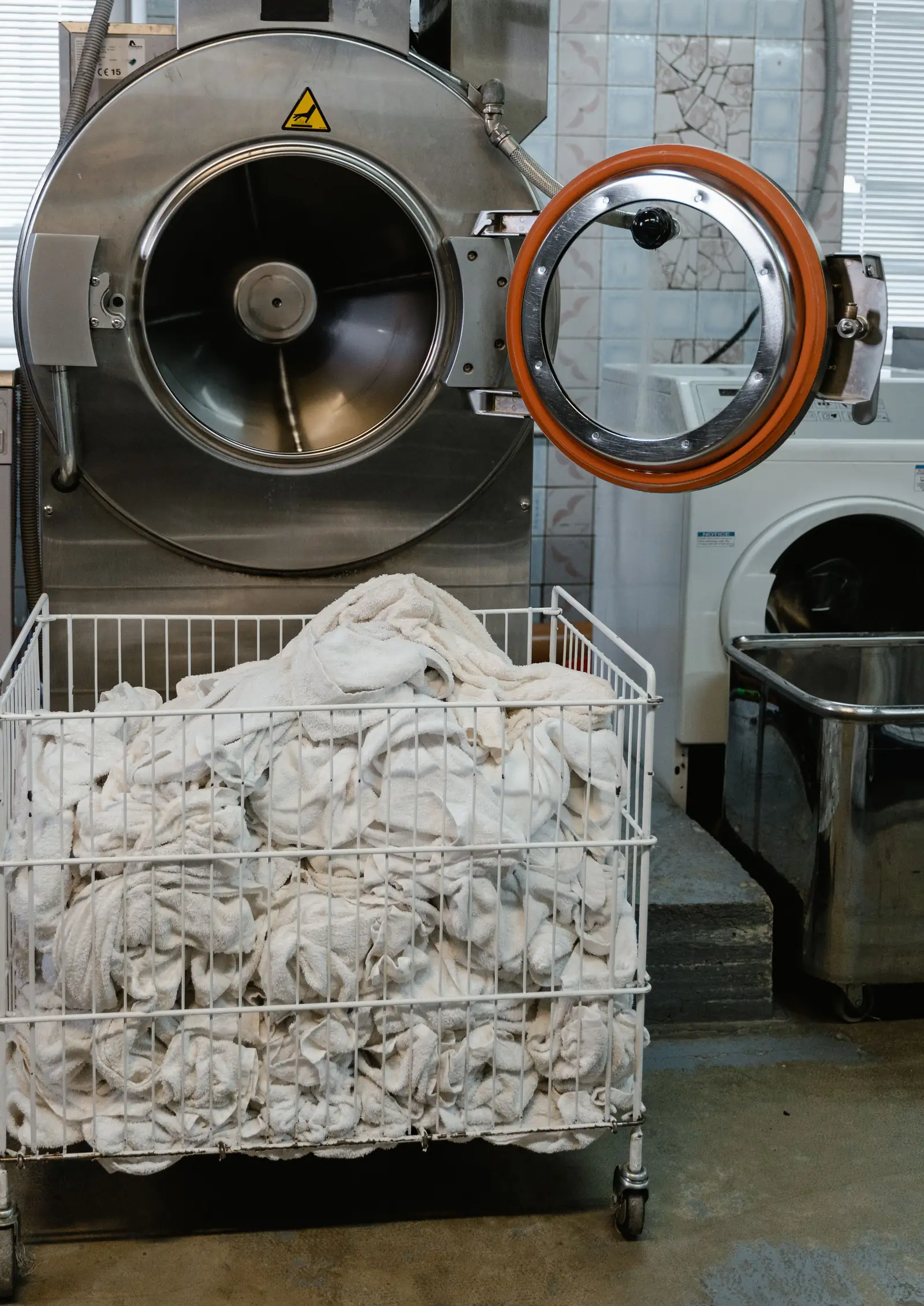 Washer-extractor with its door open beside a cart of white towels