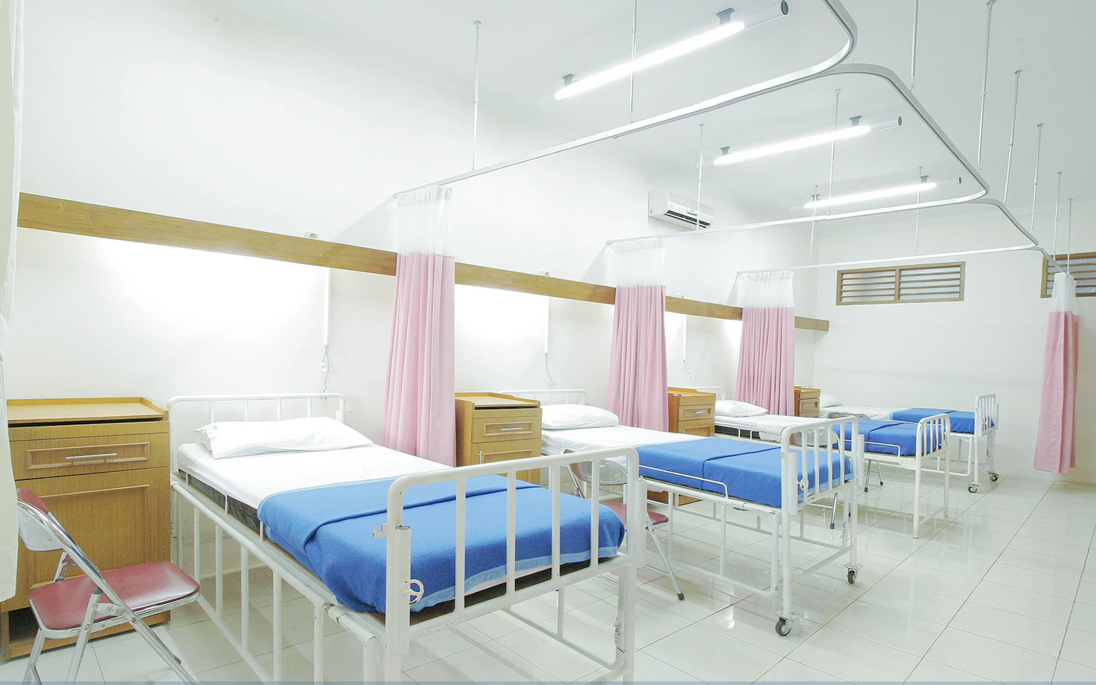 Hospital ward with made beds, blue blankets, and privacy curtains