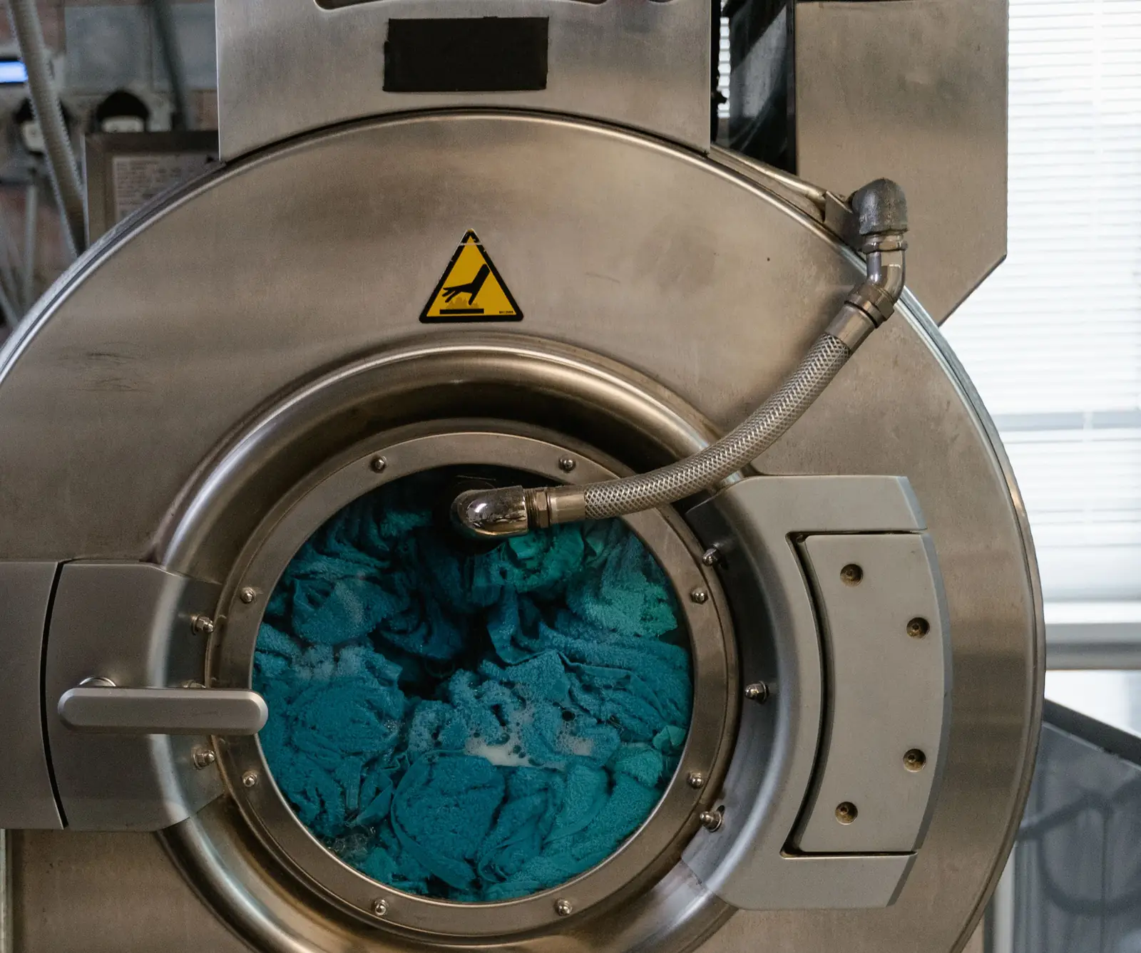 Door of a washer-extractor with a load of teal towels behind the glass