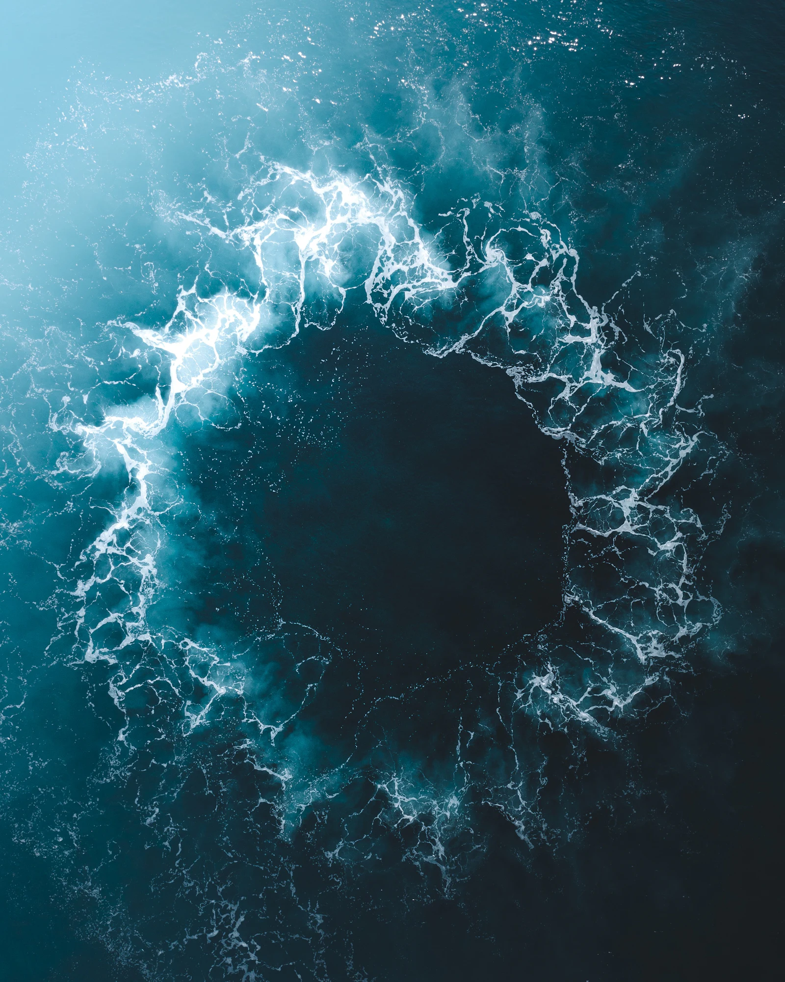 Ring of white foam on dark blue water, seen from above